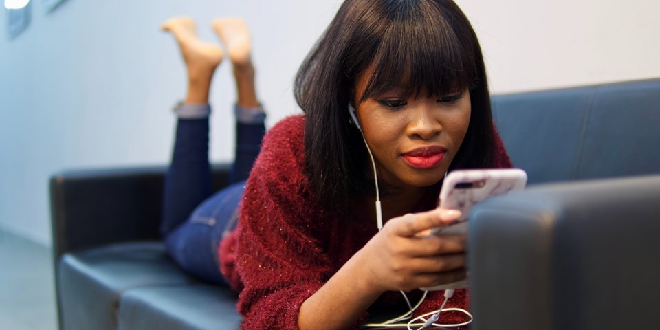 Woman lying on couch with headphones on phone